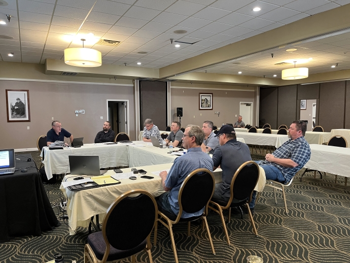 A group of people sit at tables arranged in a semi-circle.
