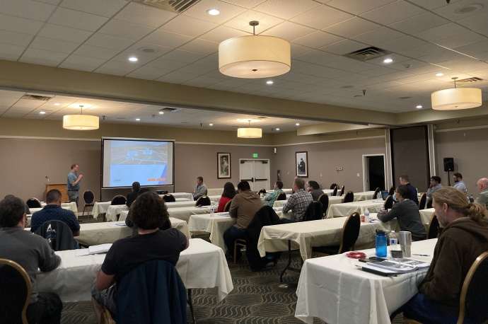Group of people seated at tables listening to a speaker in the front of the room