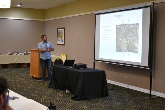 A man points at a map image displayed on a projector screen.