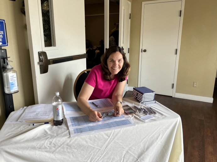A woman poses for a picture while seated at a table with a registration sheet in front of her.