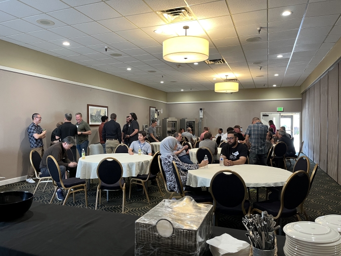 Small groups of people talk to one another while standing near equipment and seated at tables.
