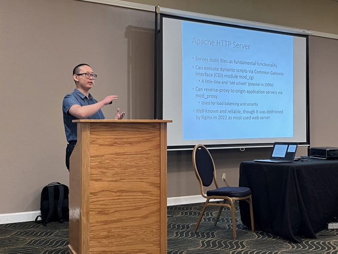 A man stands behind a podium and gestures at a projector screen behind him. Text on the slide includes Apache HTTP Server.