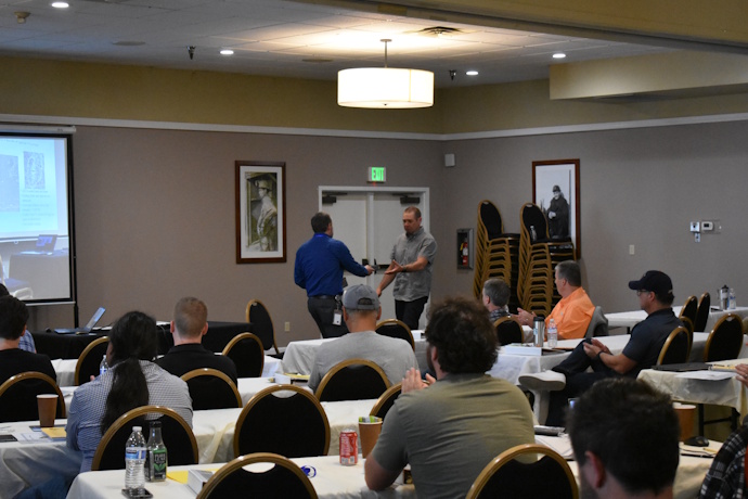A man hands a box to another man while an audience looks towards them.