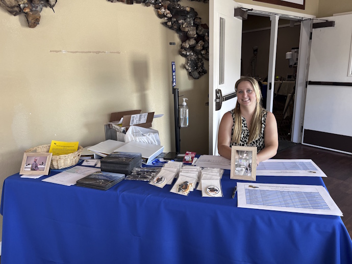 A smiling woman with long, straight blonde hair seated behind a table covered with Forum branded materials.